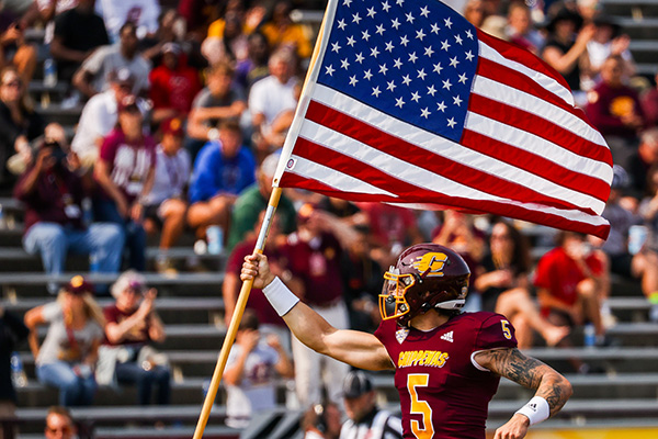 A football player holding the United States flag on the football field.