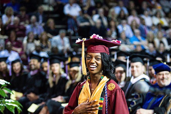 A female student at the graduation ceremony smiling while wearing her cap and gown.