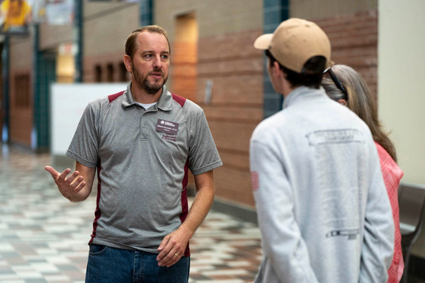 A Central Michigan University faculty member, in a gray polo, talks with a group of students in the hallway of the CMU Engineering and Technology building.