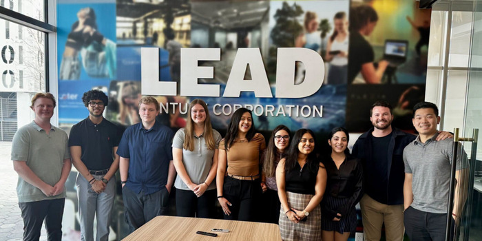 giving_connectivity_700x350 A diverse group of ten CMU students posing together in front of a wall featuring a large LEAD display and photo collage.