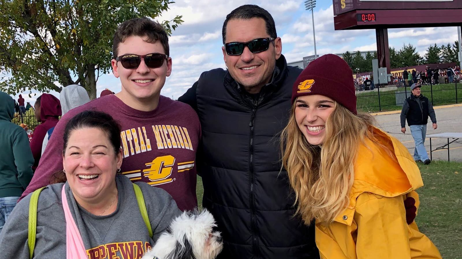 A group of four people pose for a picture outside of a football field.