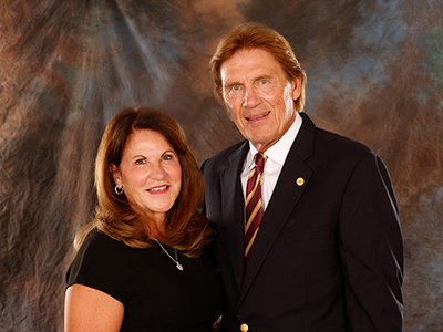 A woman with red hair stands with a man in a suit coat and maroon and gold tie.