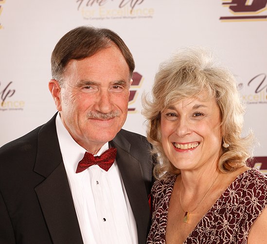 A man in a maroon bow tie stands with a woman in a maroon dress.