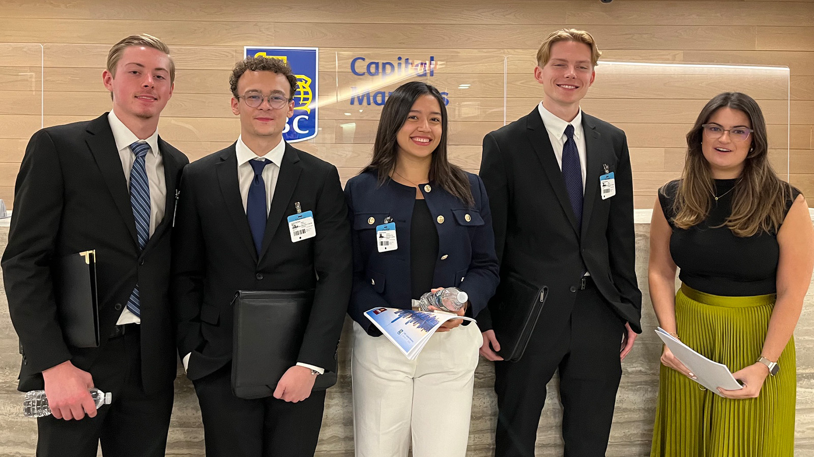 RBC group 1600x900 A group of college students dressed up in professional clothes stand in front of a wall.