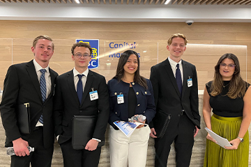 A group of college students dressed up in professional clothes stand in front of a wall.