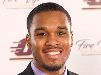 A young man stands in front of the alumni backdrop.