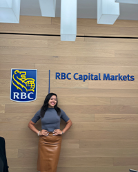 A woman standing in front of a logo to her left that reads RBC and a sign over her right that reads RBC Capital Markets.