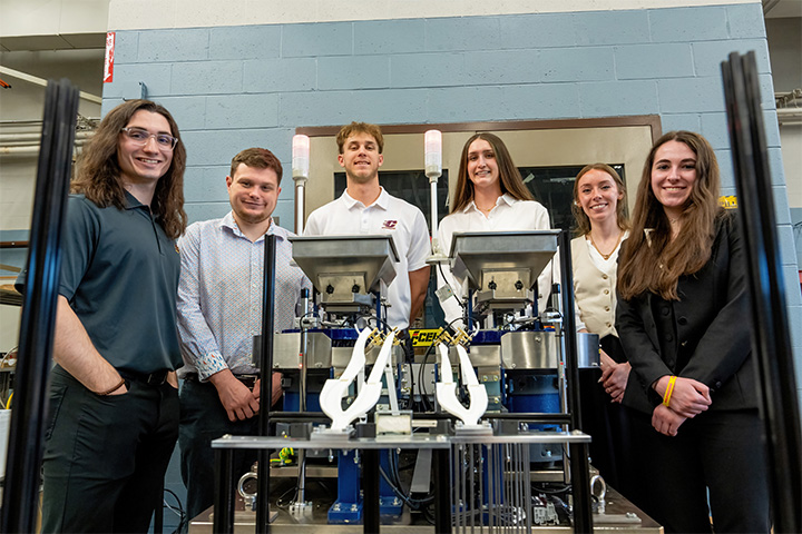 A group of people stand beside and behind a transmission machine.