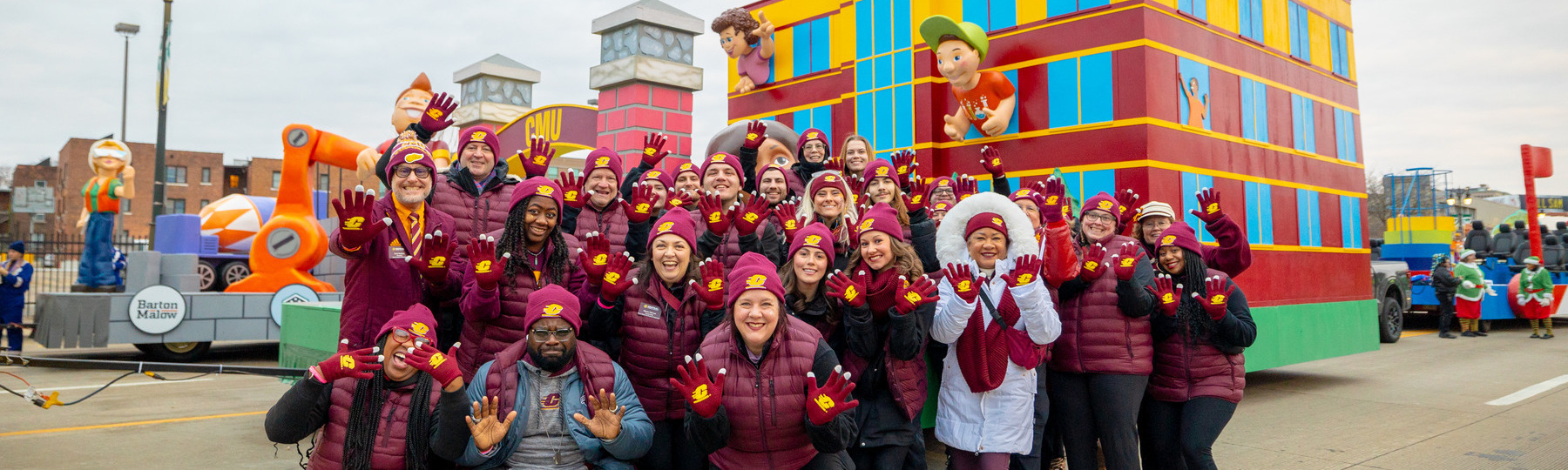 Alumni staff and community, in CMU gear, pose in front of CMU Thanksgiving Day Parade floats.