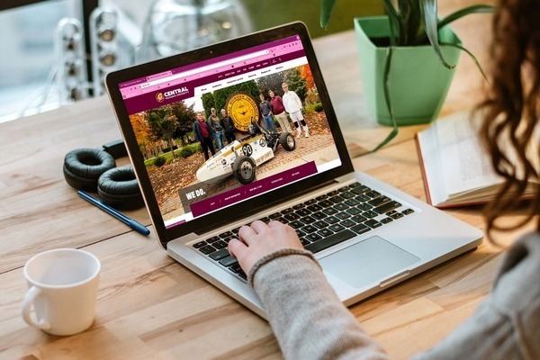 A person at a desk using a laptop displaying the Central Michigan University website.