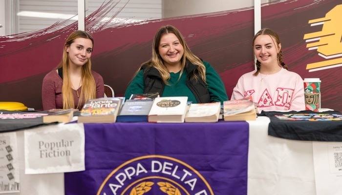 CMU Kappa Delta Pi sorority members pose behind a desk at a recruitment event.