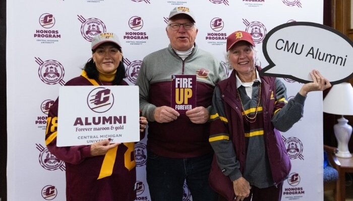 Honors Alumni pose in front of a photo backdrop with the Honors Program logo.