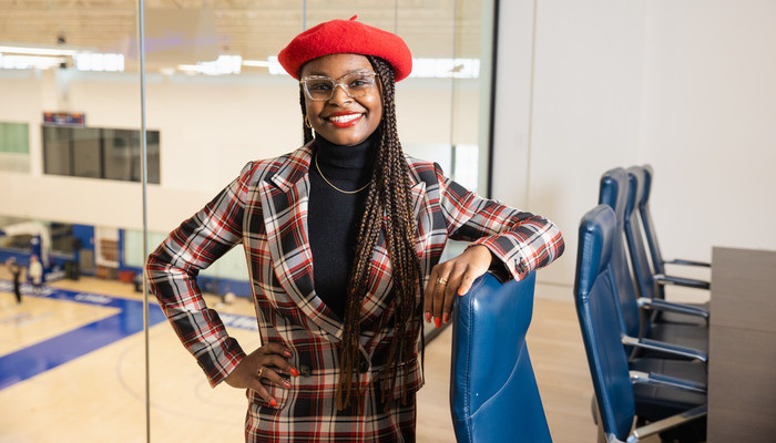 alumni_inaction_700x400 A Central Michigan University alumna posing in a plaid suit and red beret in a modern office setting.