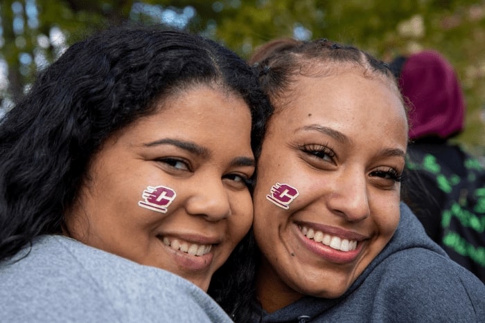 Two women with Action C stickers on their cheeks smile at the camera.