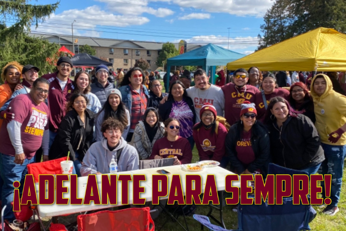 A large group of people stand outdoors at the 2022 Latine Alumni Tailgate. There is text on the image that state Adelante para sempre which translates to Fire up forever.