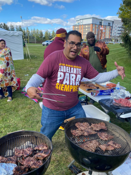 A man cooking over two grills and wearing maroon and gold.