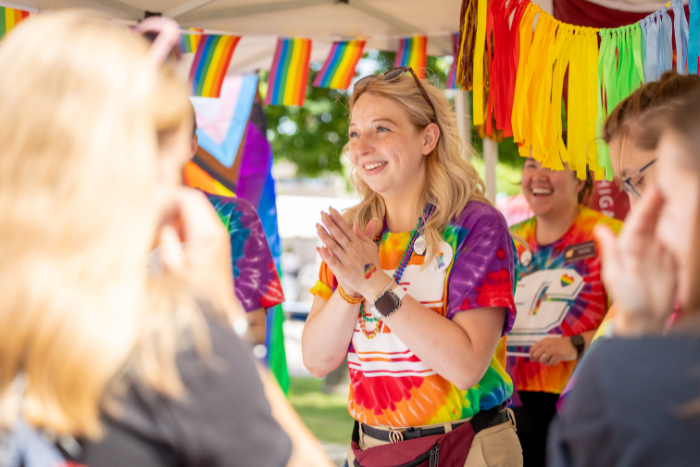 A Central Michigan University staff member in a rainbow t-shirt talks with visitors of the booth.
