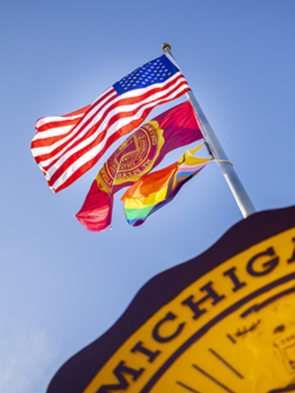 A USA flag, CMU seal flag, and LGBTQ Pride flag fly above the President's Seal on Warriner Mall.