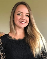 Brooke Gow's headshot for the Alumni Awards where she is wearing a black lace top and has long blonde hair while smiling with teeth.