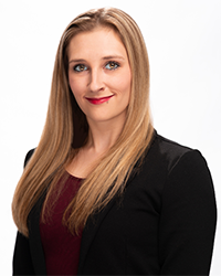 Karie Herringa's headshot for the Alumni Awards wearing a black blazer and maroon top with long blonde hair and smiling.