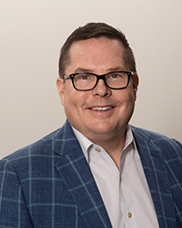 Bob Oros smiling for a professional headshot, while wearing glasses and a button up shirt with a suit jacket.