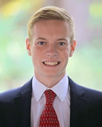 Tyler Zimmerman poses for a headshot photo with a suit and red tie.