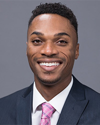 Headshot of Charles Mahone II for the 2024 10 Within 10  Alumni Awards who is wearing a dark navy suit with a pink plaid tie and he has short black hair and is smiling with teeth.