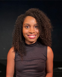 Headshot of 2024 Alumni Awards 10 Within 10 Recipient Tyler Bradley who is wearing a black mock-neck sleeveless top and she has shoulder-length curly hair and is smiling with teeth.