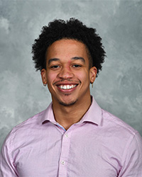 Headshot of Reginald Woods for the 2024 10 Within 10 Alumni Awards and he is wearing a purple button-down shirt and has black hair and is smiling with teeth.