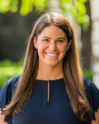 A woman smiling outdoors in a navy shirt.