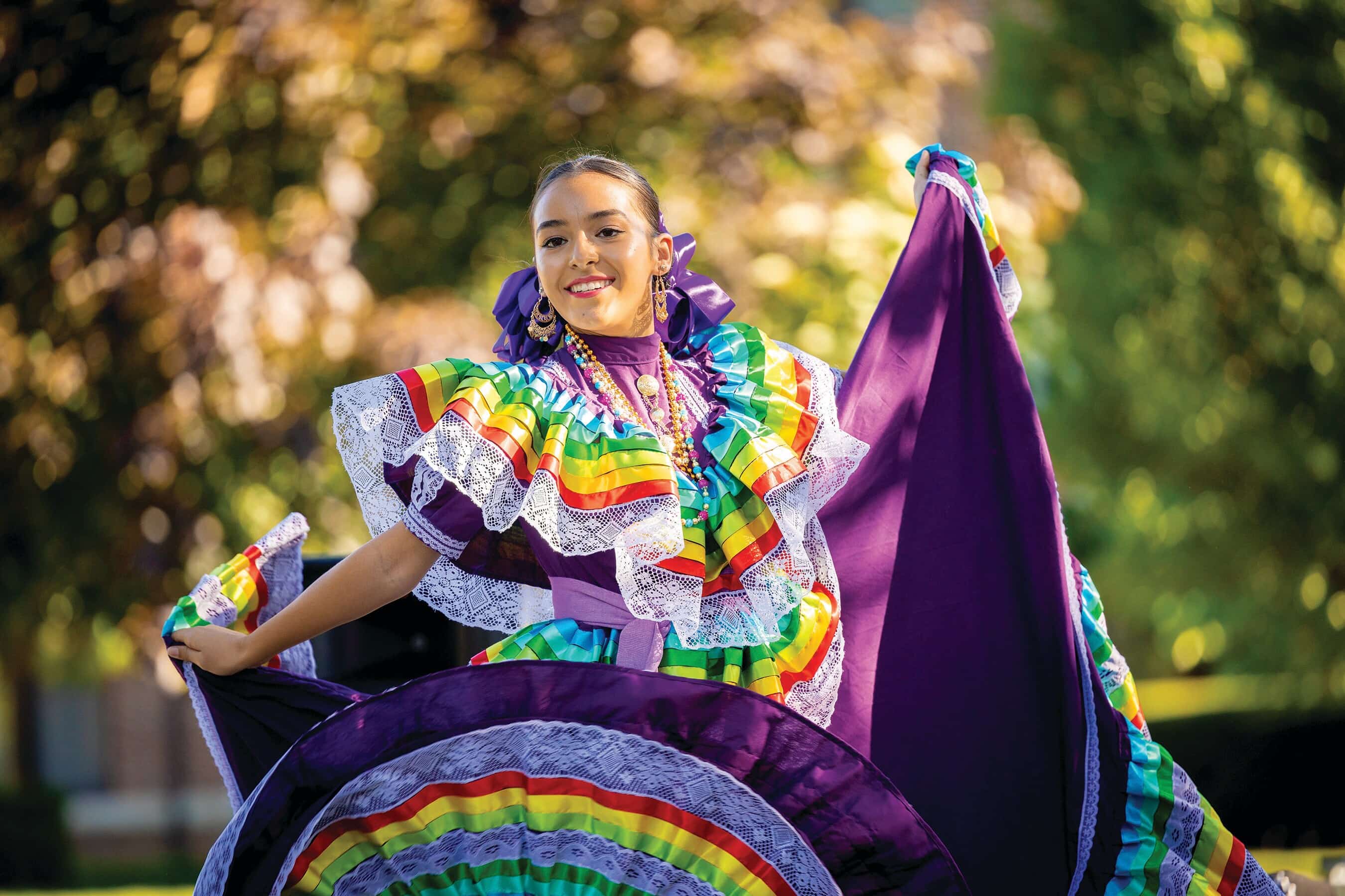 A woman in a colorful dress is dancing outdoors.