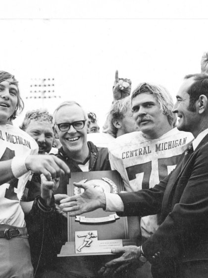 A black and white photo of CMU coaches and football players celebrating and holding a trophy.