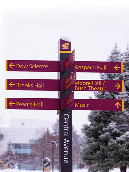 A Central Avenue sign post on the campus of Central Michigan University that indicates the directions to Dow Science building, Brooks Hall, Pierce Hall, Anspach Hall, Moore Hall/Bush Theatre and the Music building.
