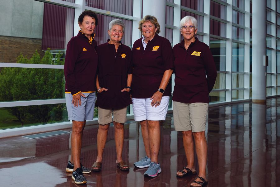 Four women wearing Central Michigan University quarter zips stand in the John G. Kulhavi Events Center.