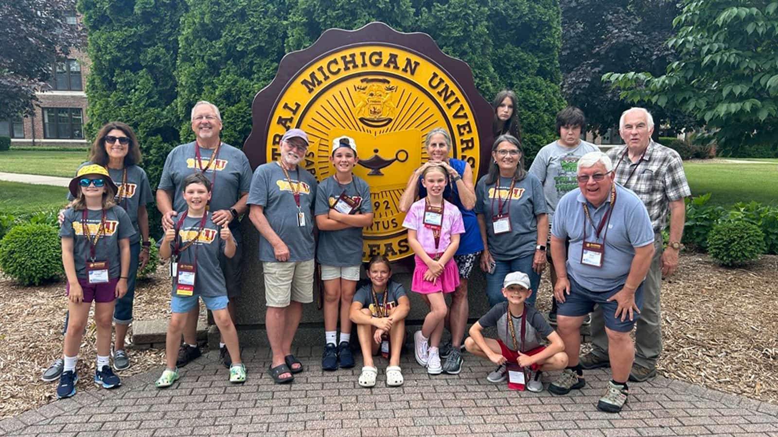 A group of people pose for a photo around the official seal at Central Michigan University.