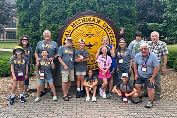 A group of people pose for a photo around the official seal at Central Michigan University.