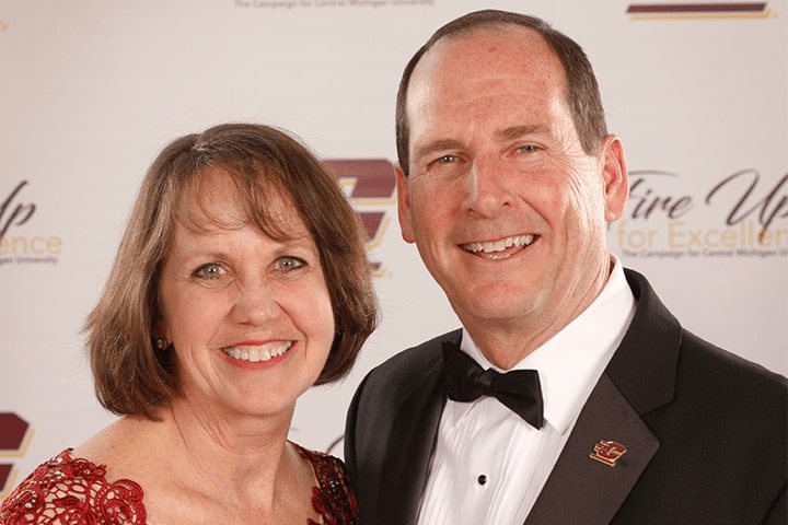 Woman in red dress with short brown hair smiles while posing with a man who has short dark hair and is wearing a tuxedo.