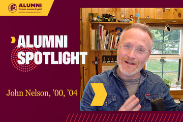 Central Michigan University Alumni Spotlight graphic for John Nelson, class of 2000 and 2004, smiling in a denim shirt in front of a pine wall, bookshelf and window.