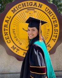 Dr. Kristen Carrillo-Kappus smiling in a graduation cap and gown with a green medical academic hood, standing in front of the Central Michigan University seal.