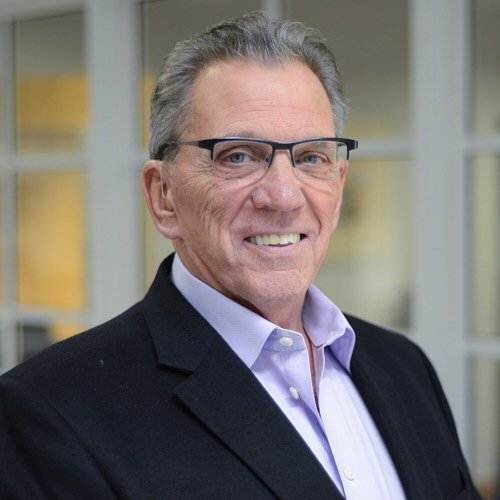 W. Sidney Smith is wearing a suit jacket and purple collared shirt with glasses.