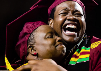 A mother and son embrace in an emotional hug in their graduation attire.