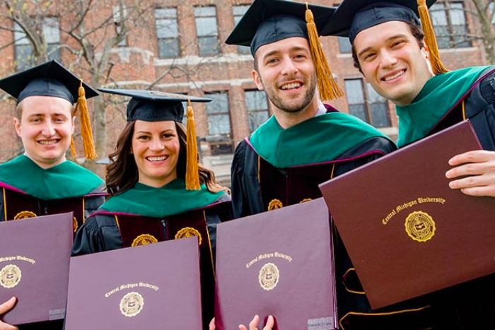 Four masters graduates holding their diplomas in a maroon case.