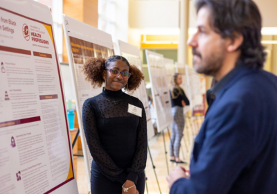 A woman presenting a research and a man observing the posterboard.