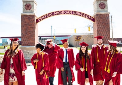 CMU graduates in caps and gowns walking together under the arch on CMU's campus.