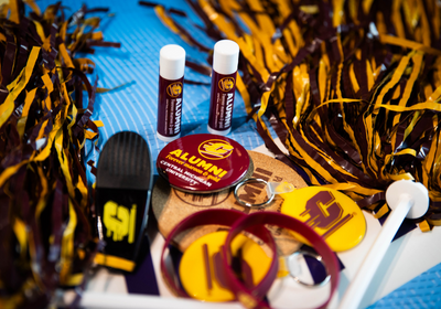 Central Michigan University Alumni swag scattered on a table, including maroon and gold pom poms, buttons, and keychains.