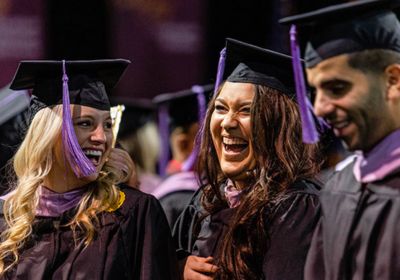 Three masters graduates smiling with black gowns and purple tassels.