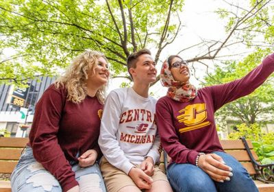 Three individuals wearing Central Michigan University shirts take a selfie.