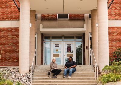 Two women chatting on the stairs of Anspach Hall entry.