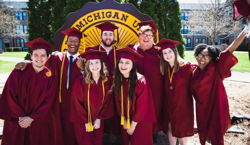 Central Michigan University graduates dressed in caps and gowns in front of the Central Michigan University seal.