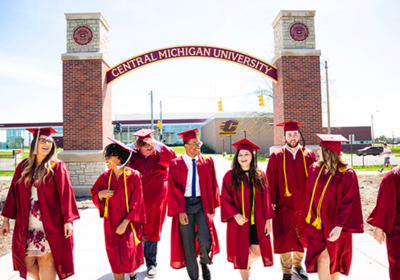 A group of individuals graduating from Central Michigan University take a photo near the arch on campus.